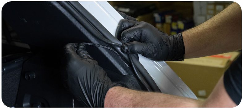Gloved hands lifting the weather strip to route the tail light harness through the hatch wiring loom on a VW Golf