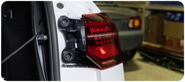 New LED outer tail light being offered up to the quarter panel of a VW Golf with the two bolt bosses visible